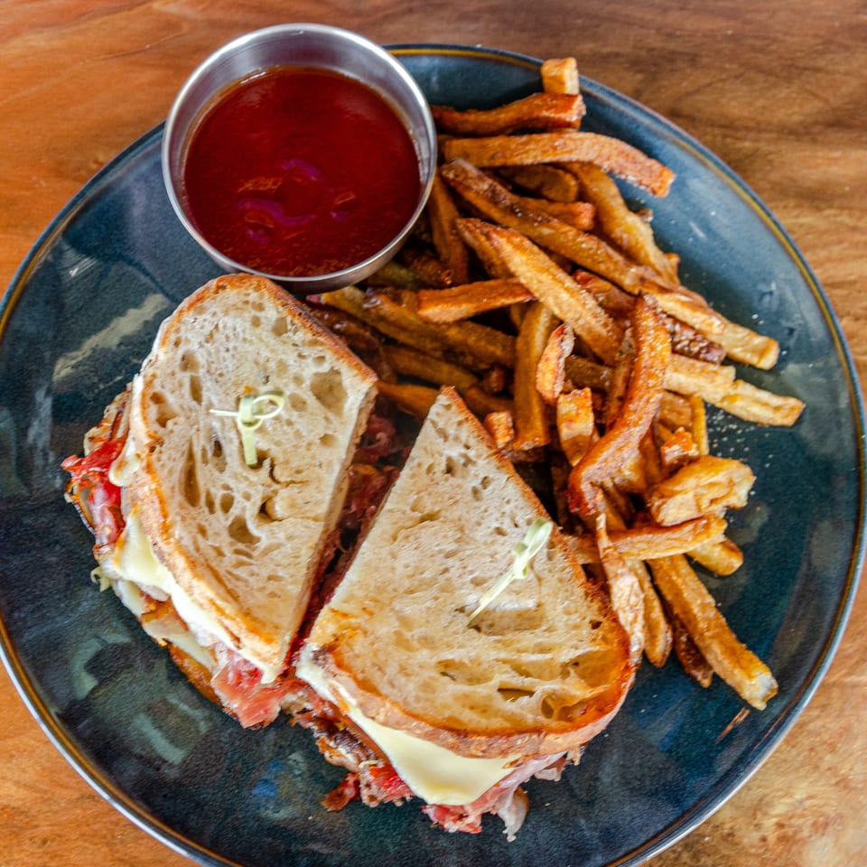 Toasted sandwich with melted cheese, fries, and a cup of red dipping sauce on a dark plate.