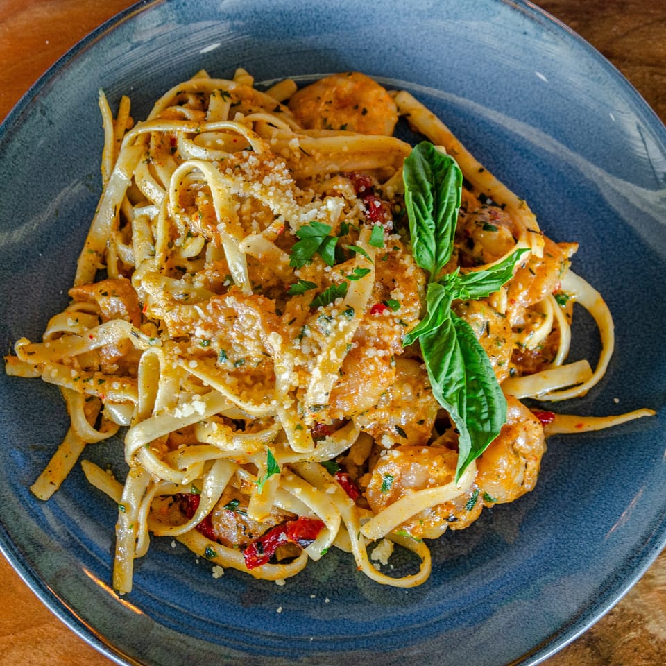 Creamy fettuccine pasta with shrimp, sun-dried tomatoes, Parmesan, and fresh basil on a blue plate.