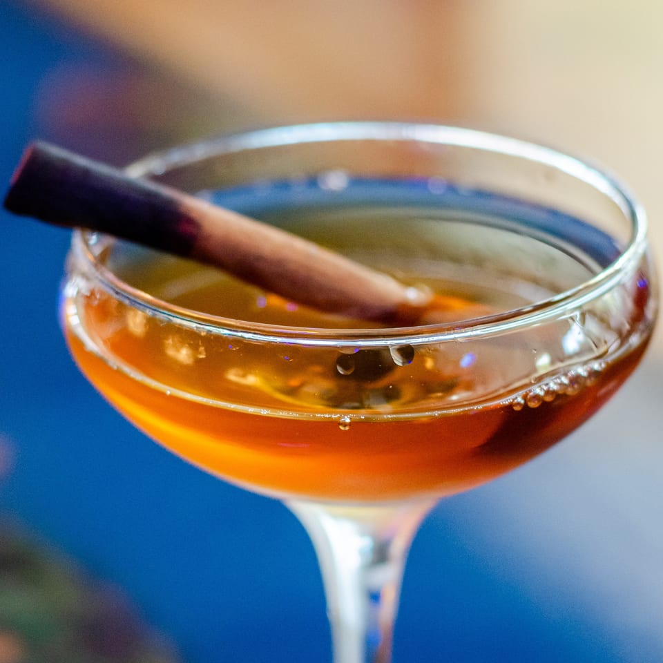 Close-up of an amber cocktail in a coupe glass garnished with a cinnamon stick.